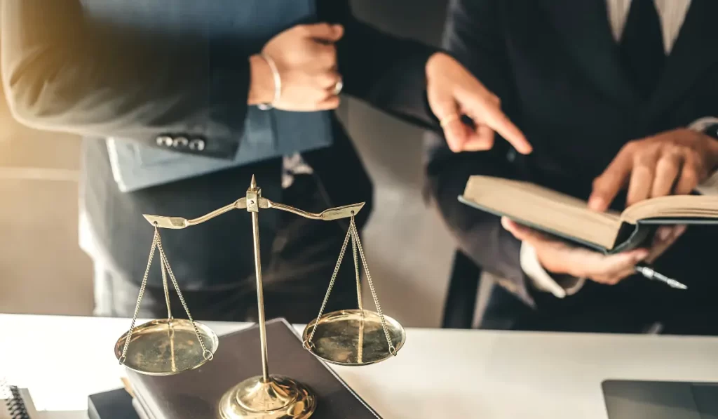 a lawyer is holding a book open while another lawyer is standing next to him in an office