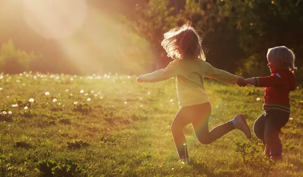 Two kids are playing in a park on a sunny day.